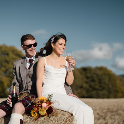 Couple sitting on a hay bale with champagne and sunglasses