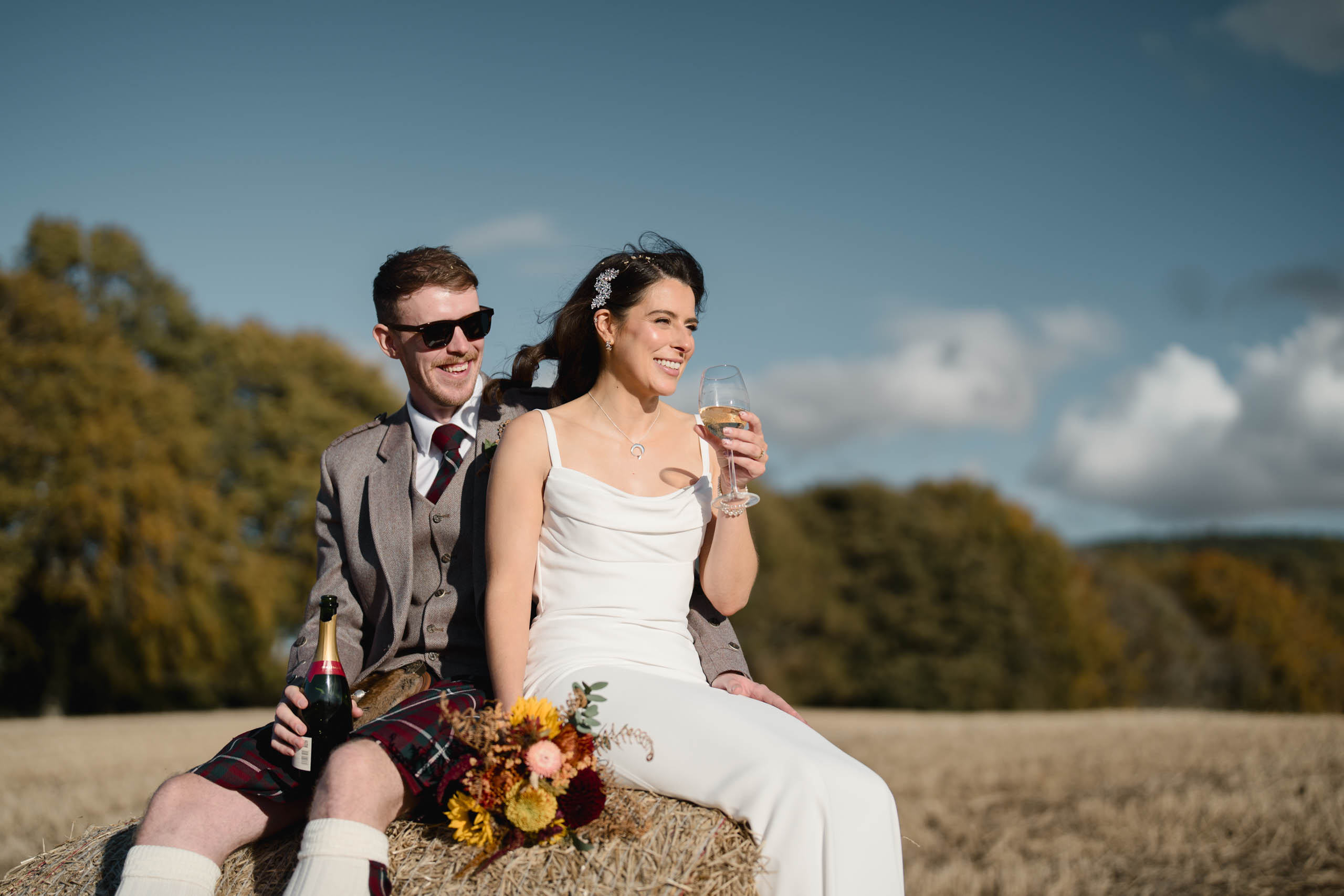 Couple drinking champagne, sitting on a hay bale at Daviot Steading