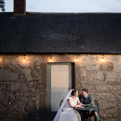Newlyweds seated outdoors under festoon lights