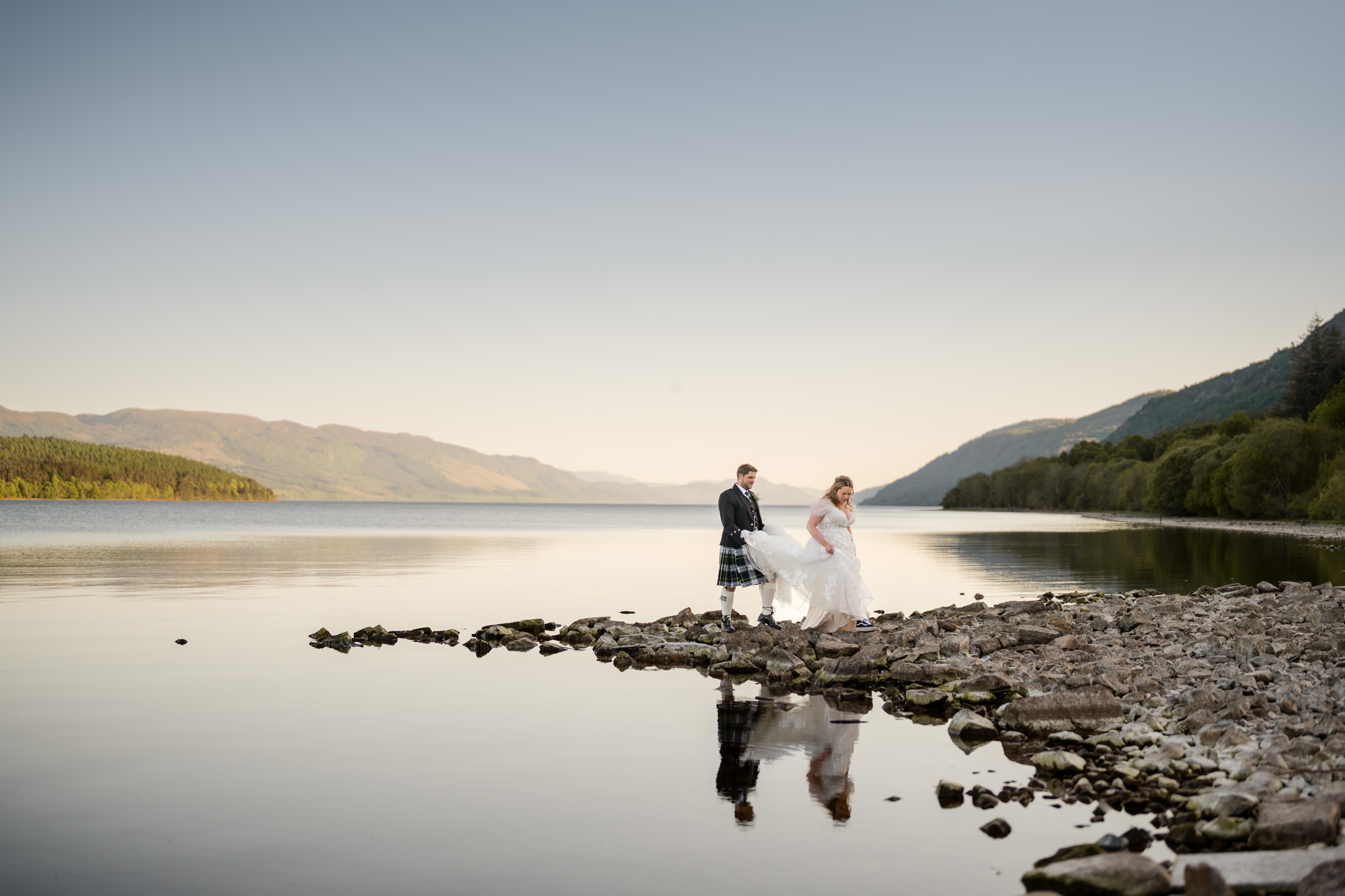 Bride and groom at Loch Ness at sunset with calm water