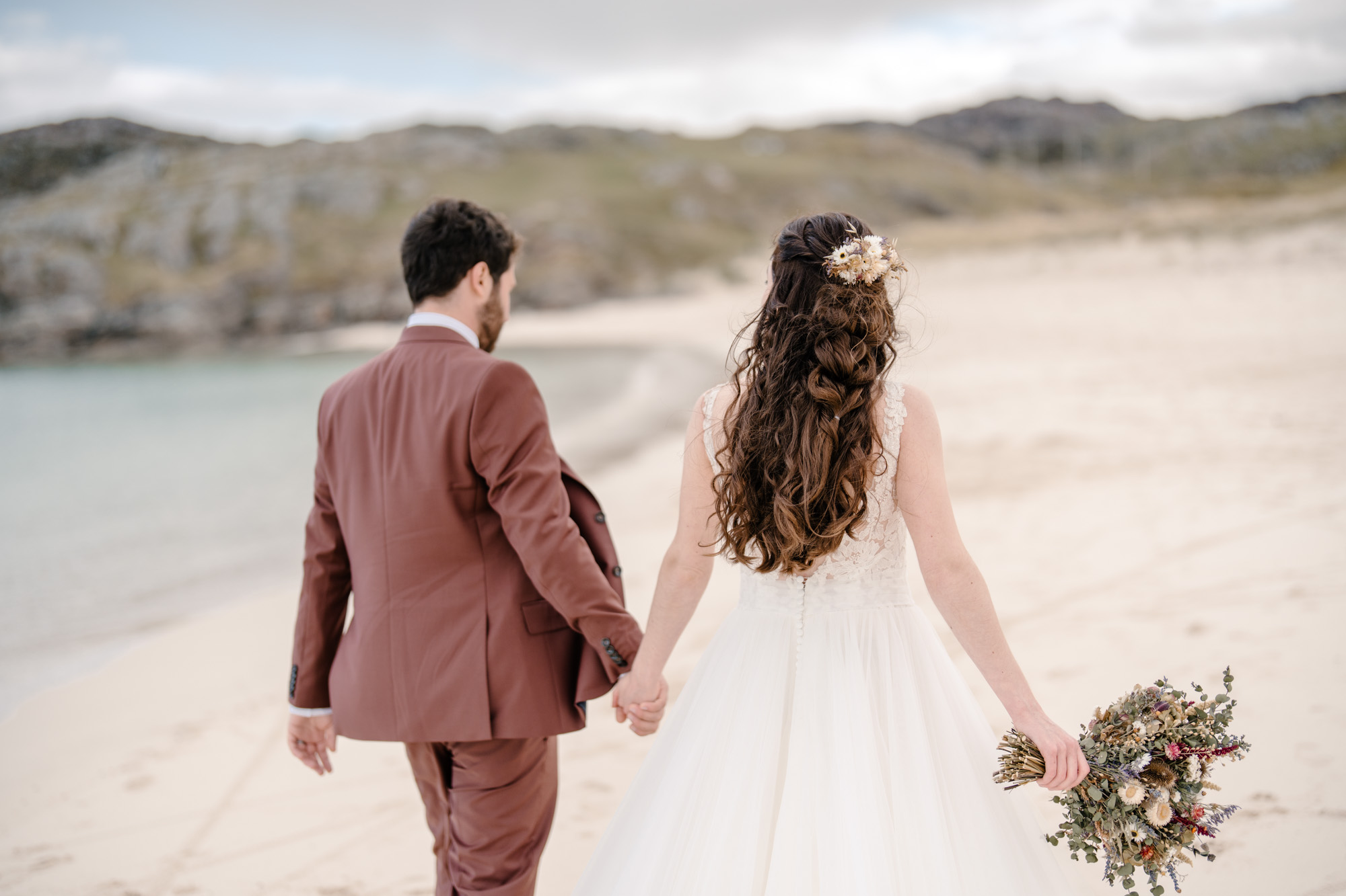 Newlywed couple walking together along a windswept Scottish beach