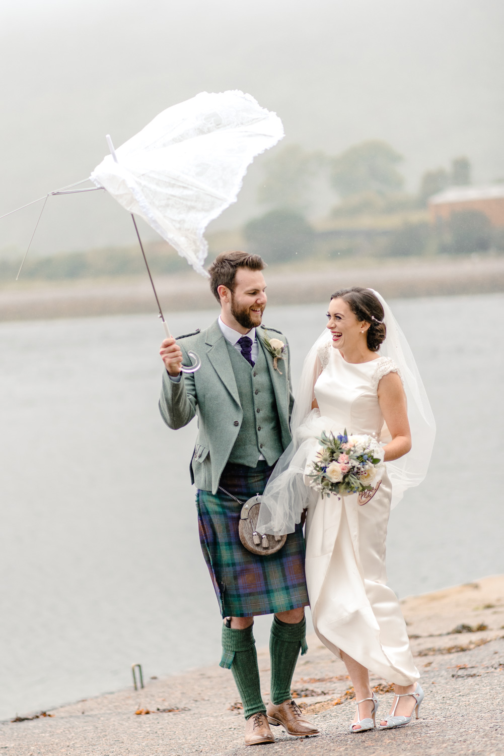 Newlyweds standing in the rain under an umbrella