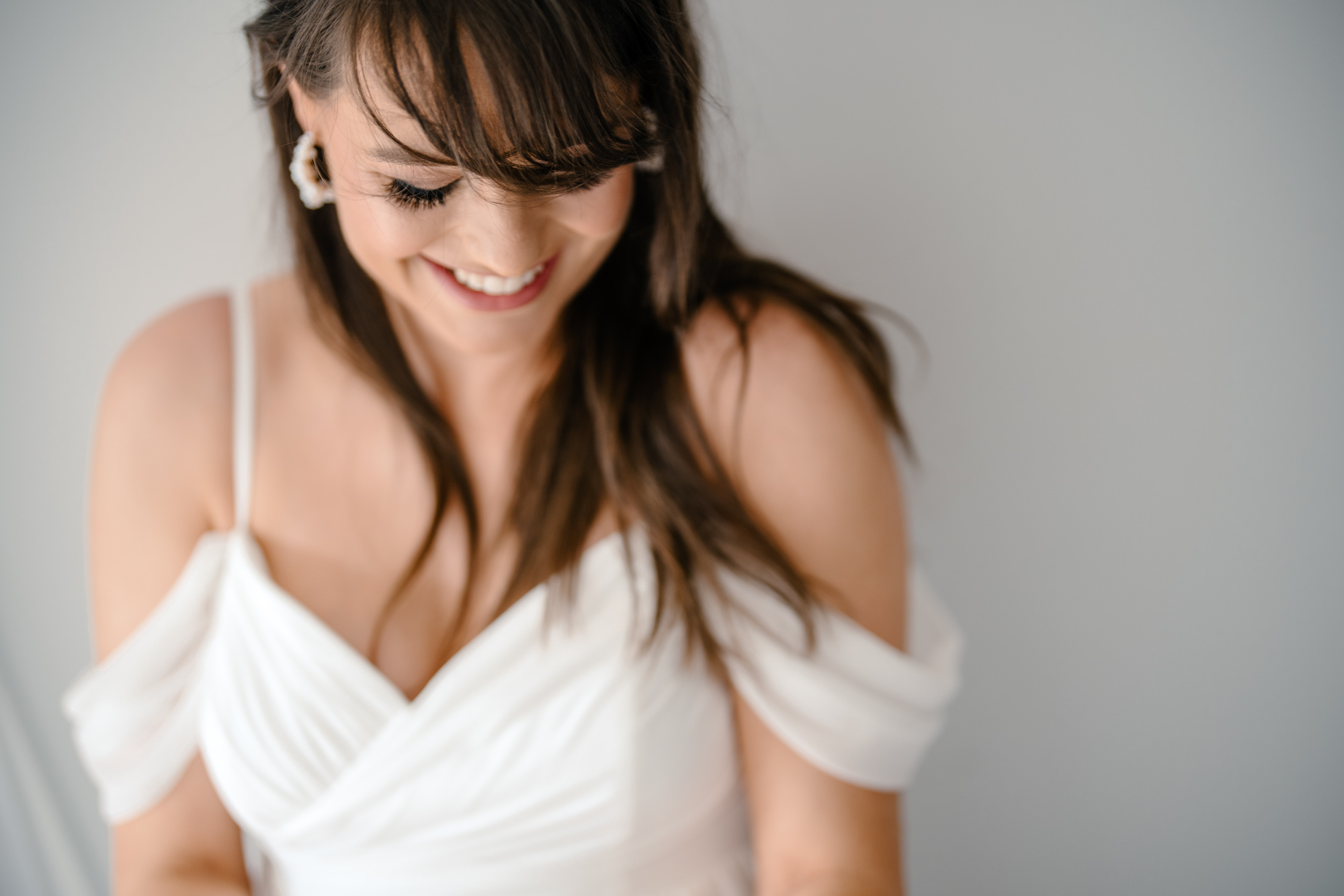Bride smiling gently, looking down in a close-up portrait with a light grey backdrop