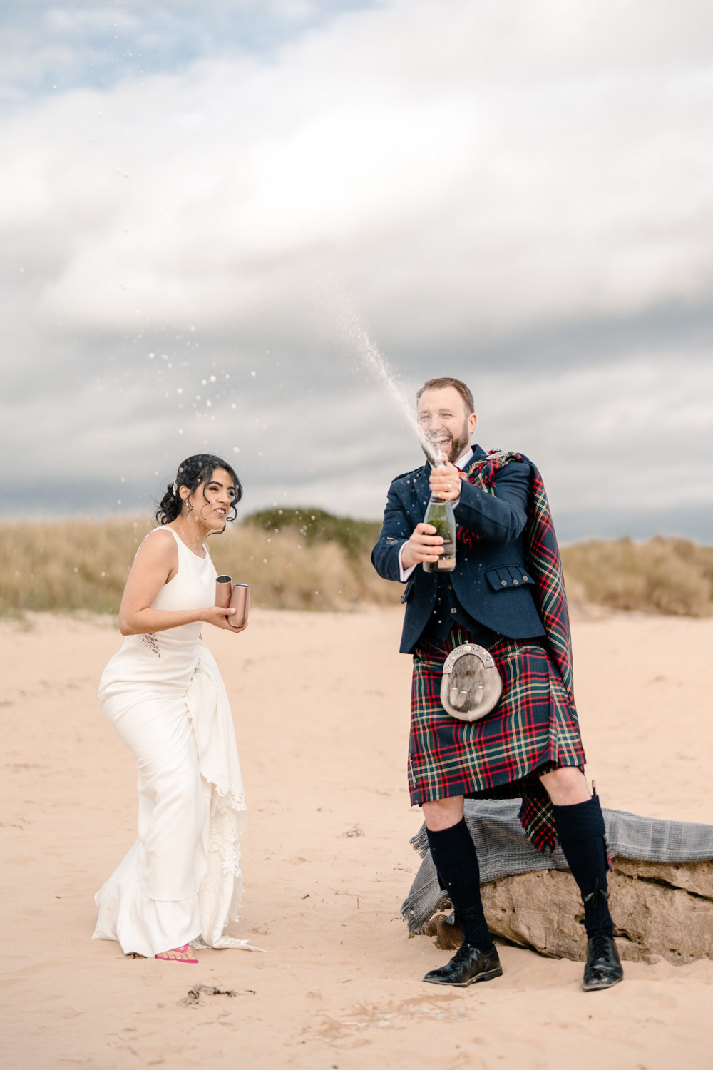 Newly married couple celebrating by spraying champagne on the beach