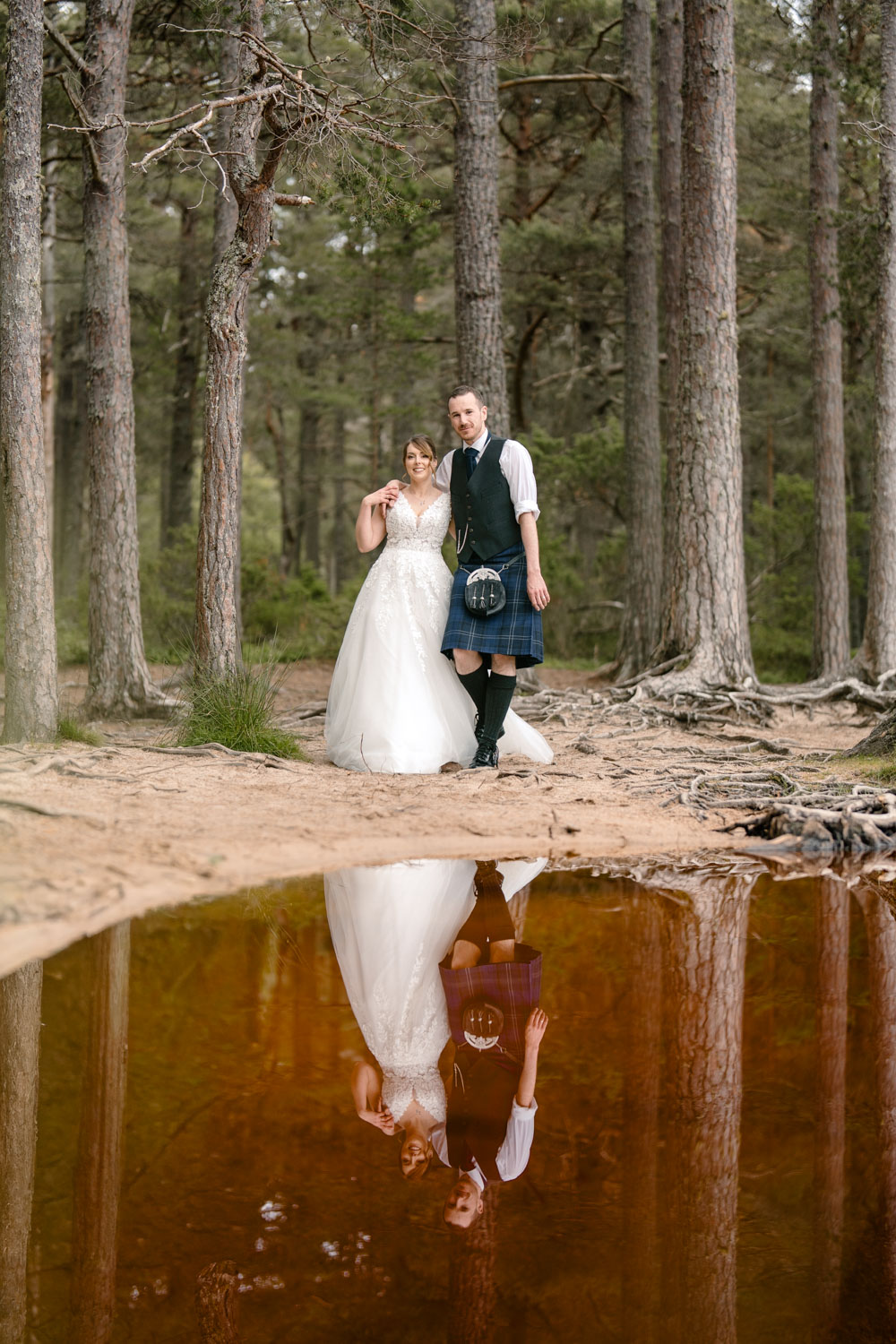 Couple walking beside a Scottish loch, reflected in the still water