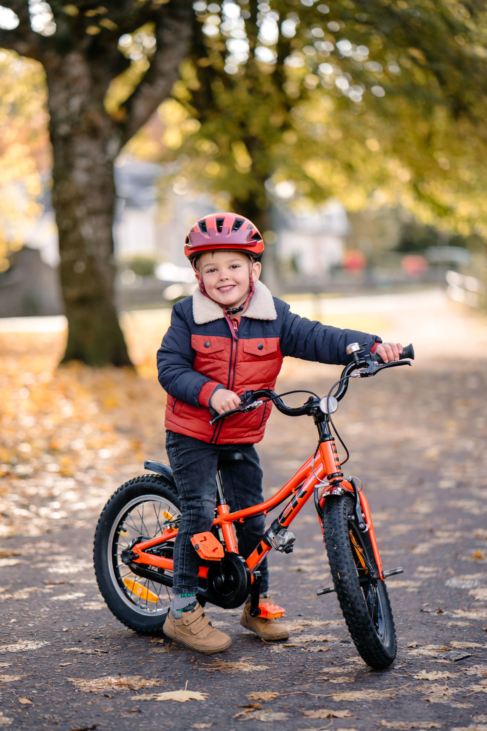 Child on a bicycle surrounded by fallen leaves in a park during autumn.