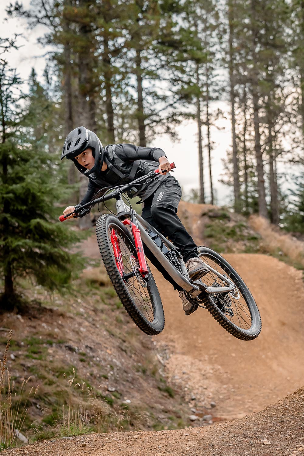 Young MTB rider airborne while jumping on a trail