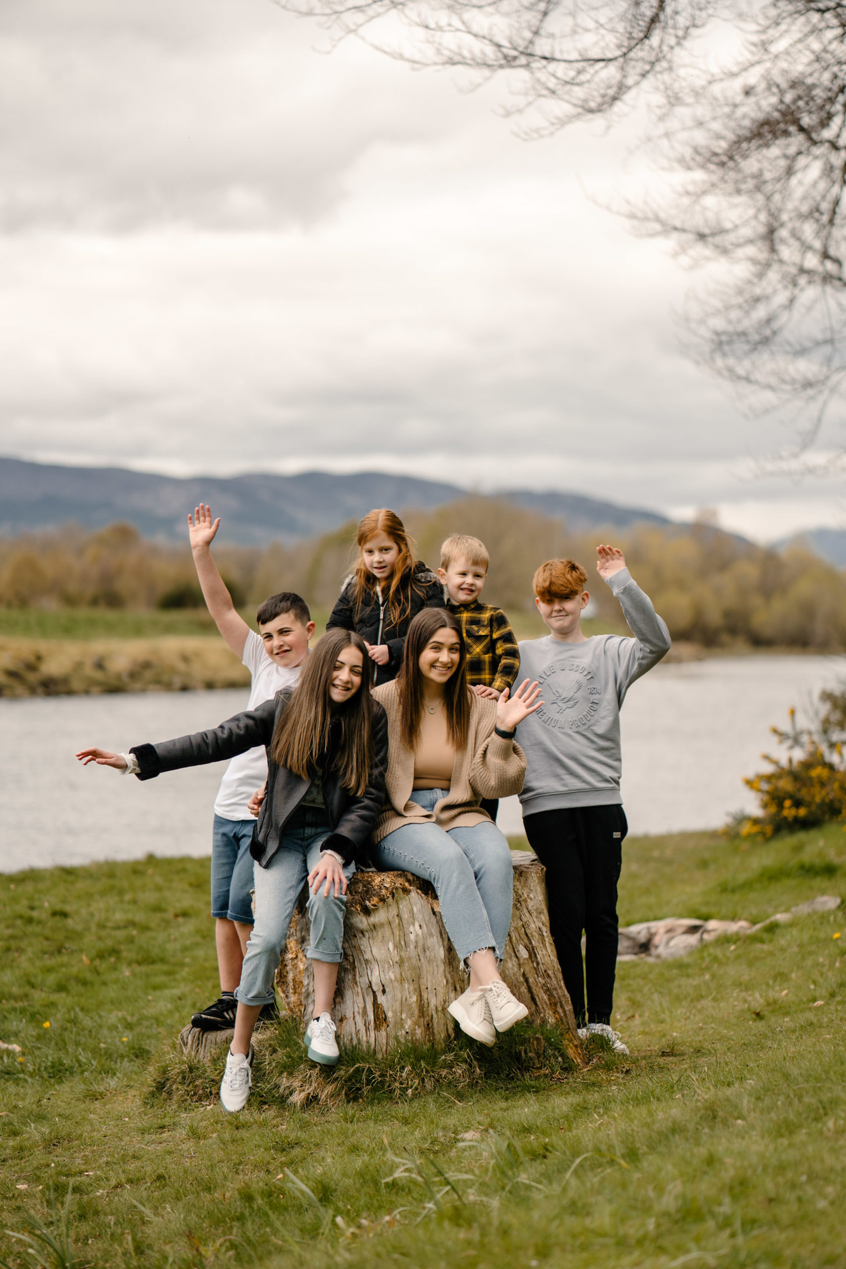 Family group enjoying a woodland setting while sitting on a tree trunk and waving.