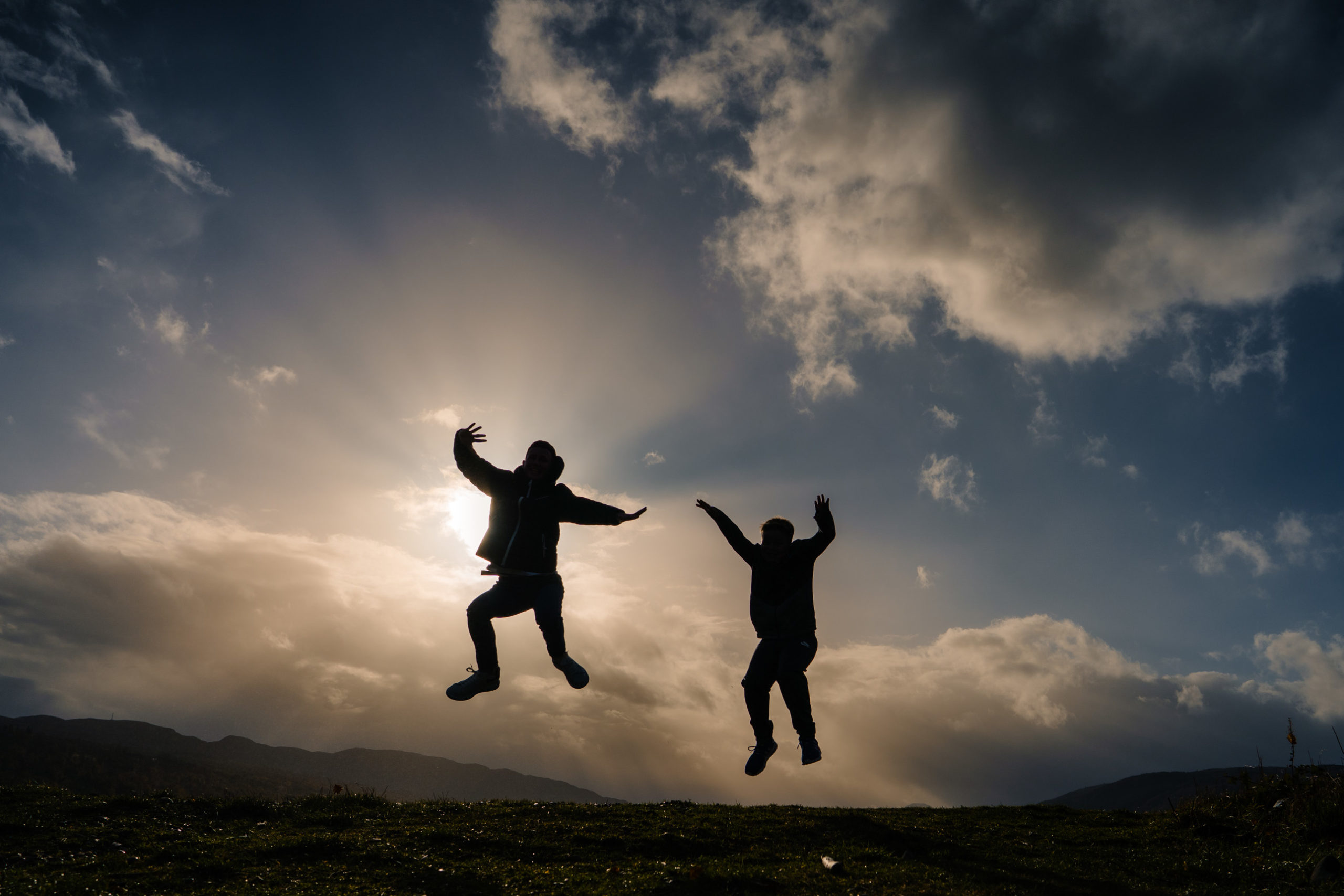 Children jumping with their silhouettes visible against a colourful evening sky.