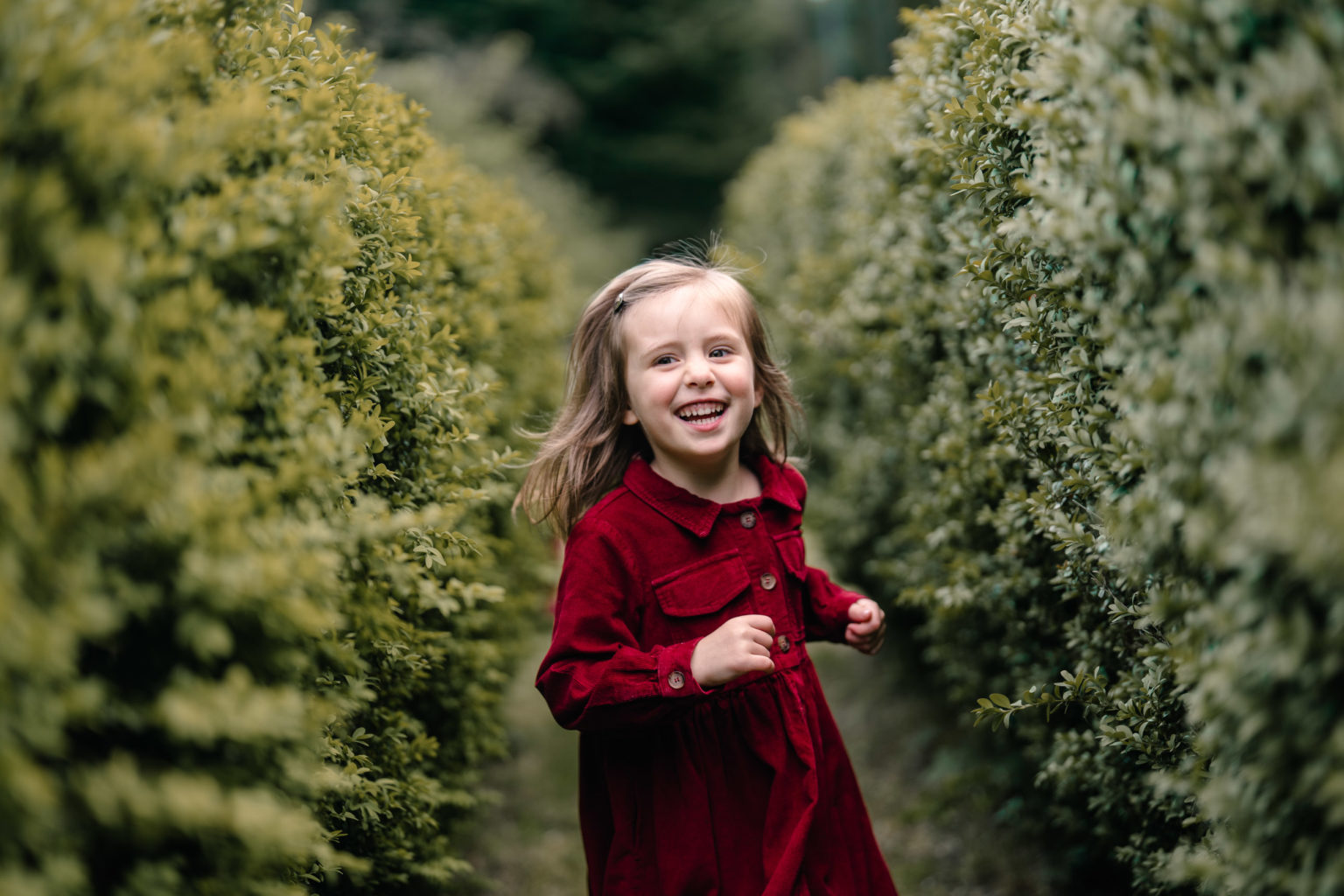 Girl laughing while running along a rural path lined with hedges.