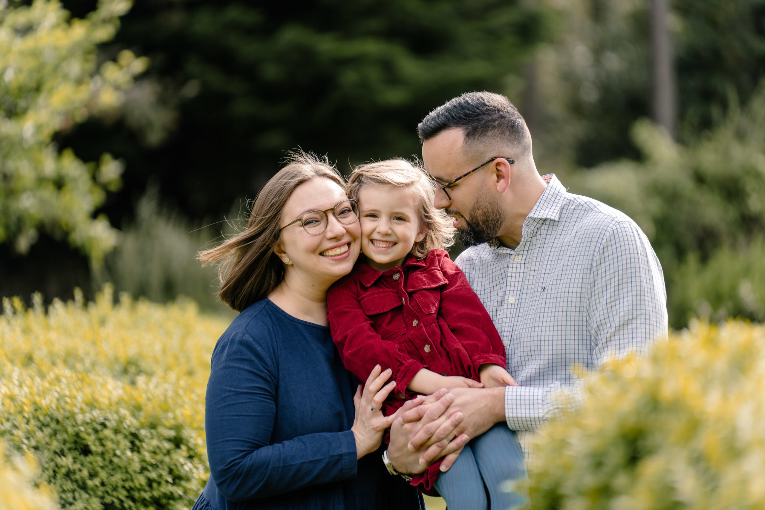 Outdoor family portrait framed by vibrant green foliage.