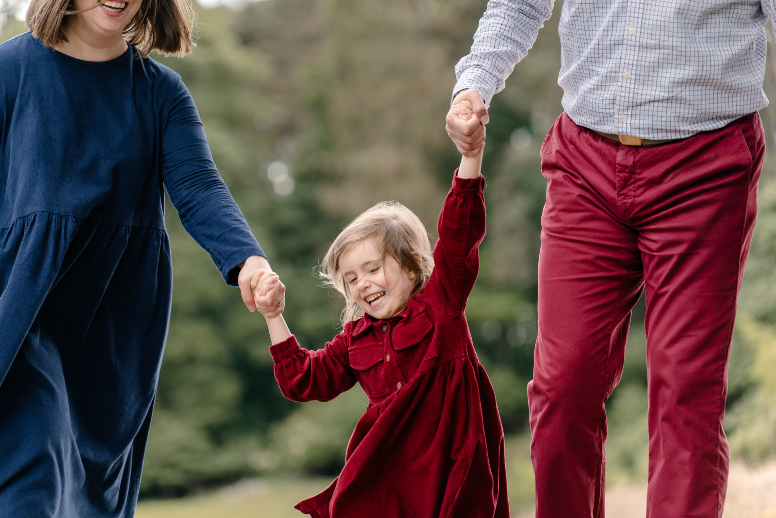 Parents swinging their daughter between them by her hands.