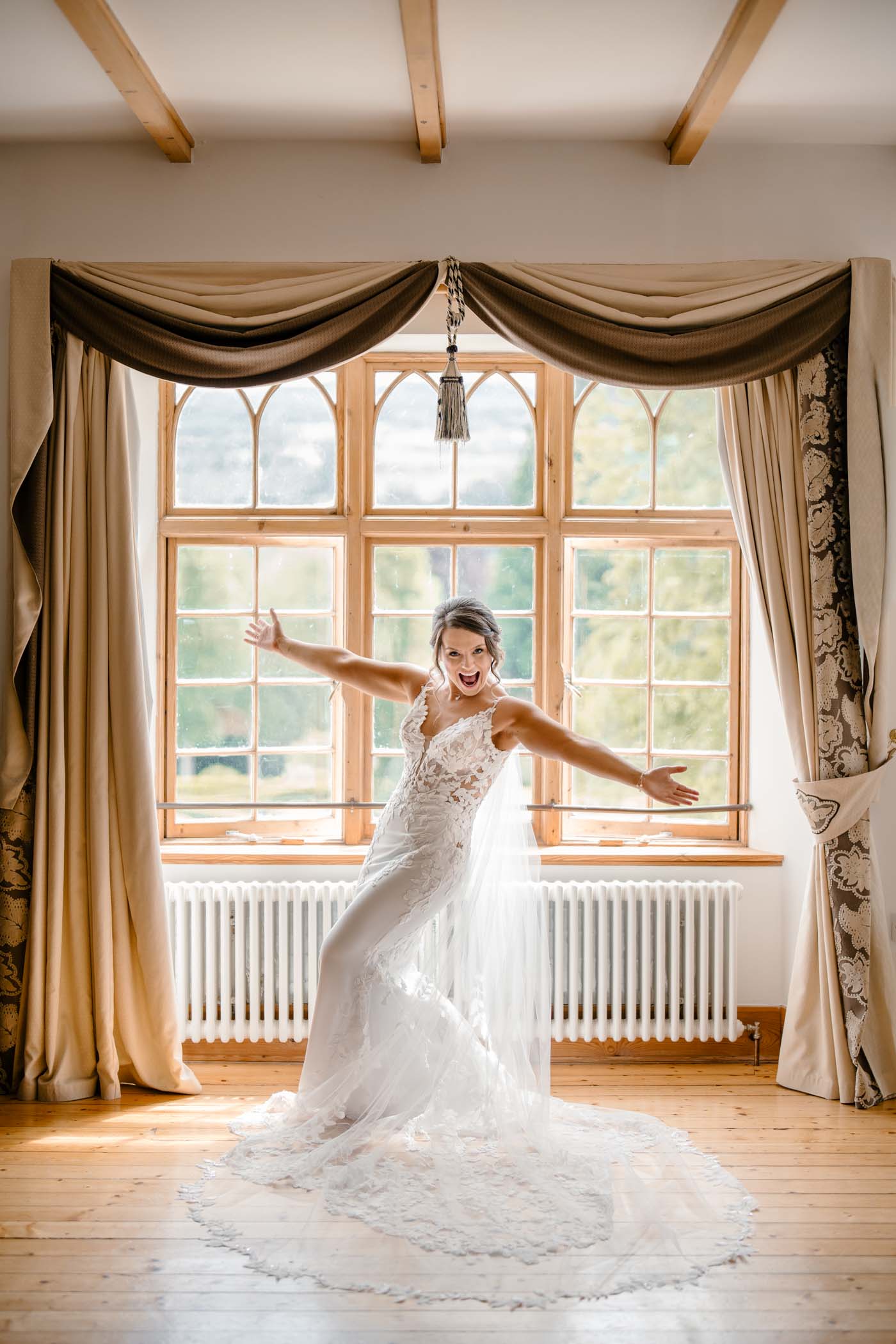 Bride joyfully standing by a window with arms outstretched