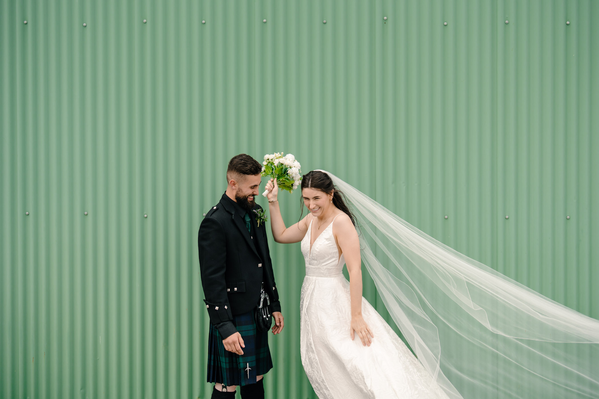 Bride and groom posing next to a green corrugated iron shed