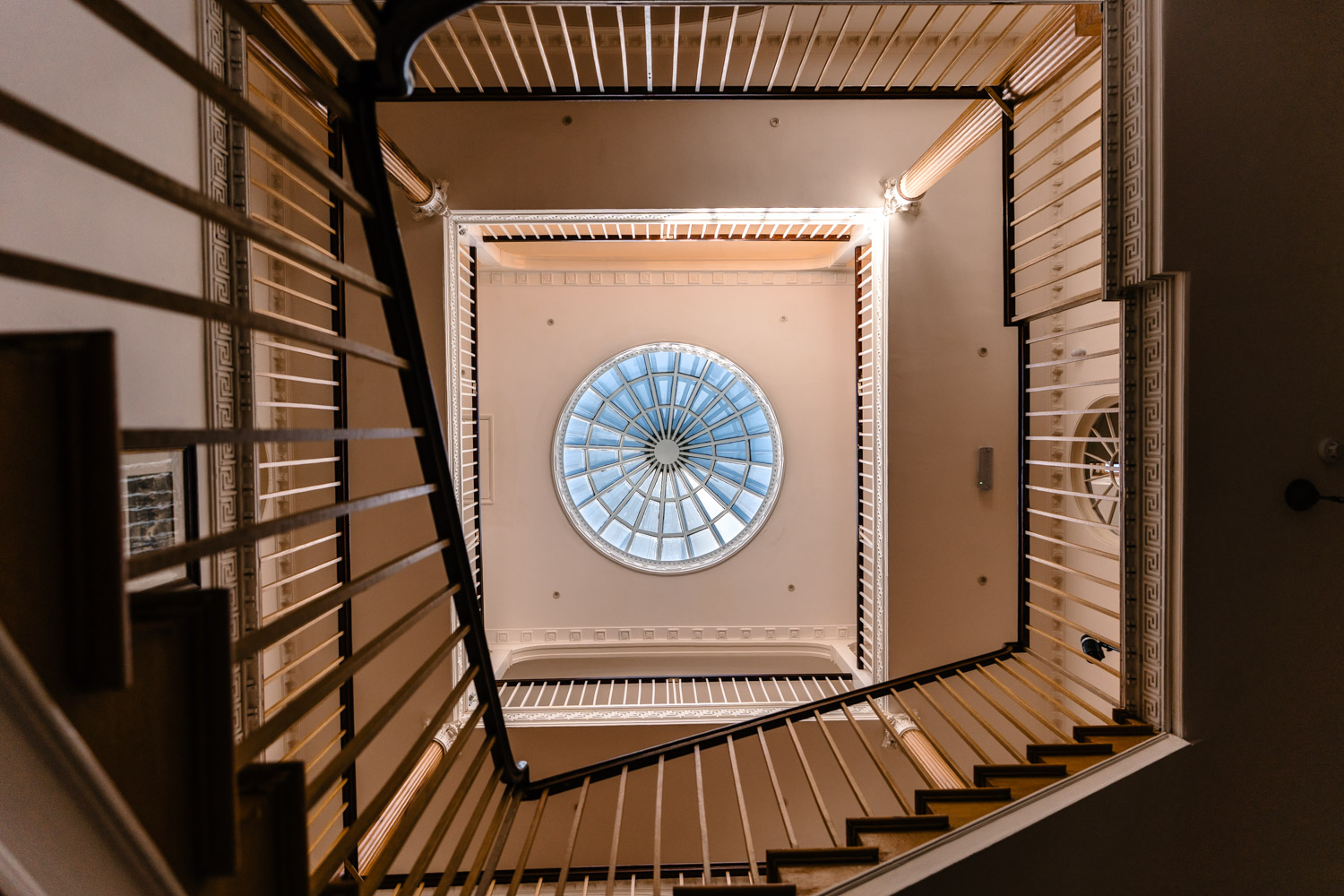 View of a staircase from ground level, leading upwards towards an impressive cupola ceiling dome that fills the space with natural light and architectural character.