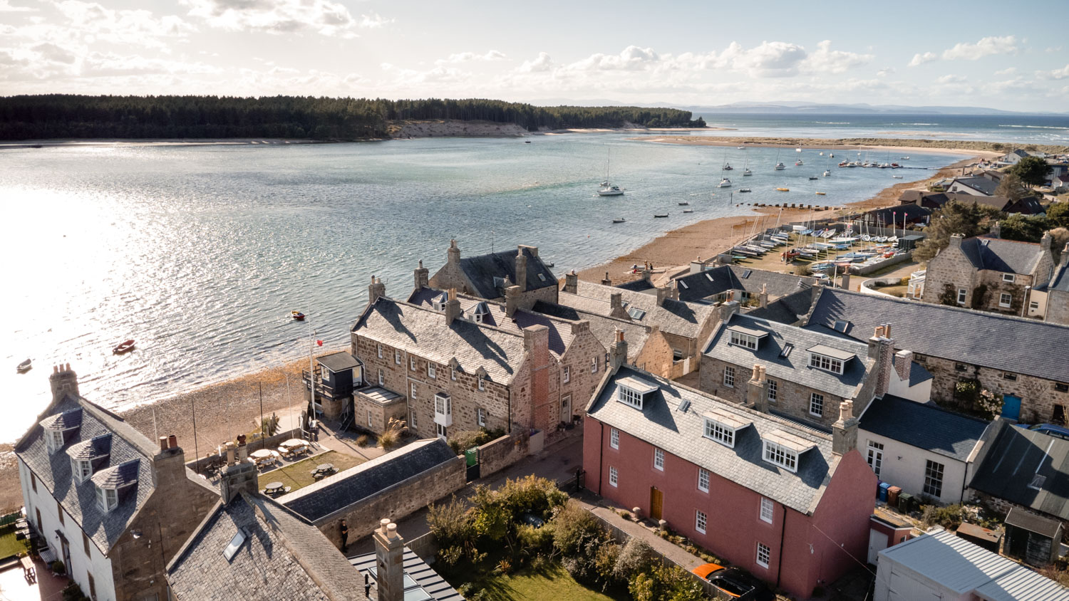 Drone view of a stone property set within its grounds, with Findhorn Bay stretching out in the background beneath open skies.
