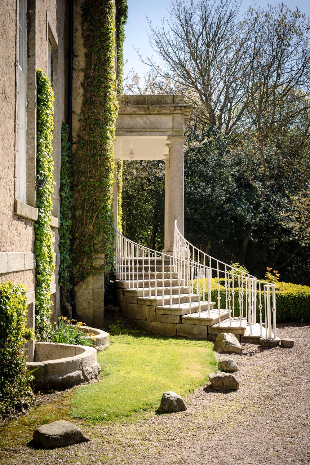 Side view of the mansion house exterior, featuring an elegant entrance framed by traditional pillars and set against the surrounding grounds.