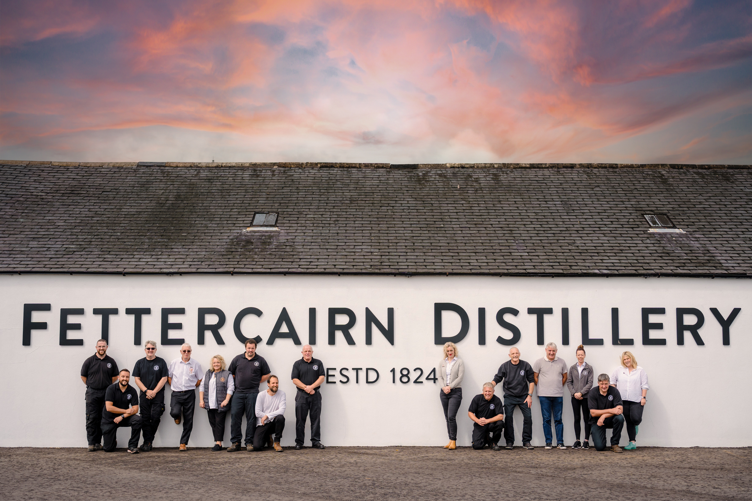 Team photograph taken at Fettercairn Distillery, with the group posed together in front of the distillery buildings.